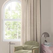 Okno z kolorową zasłoną w kwiaty w czerwieni, pomarańczu i błękicie, zielony fotel i mały stolik z lampą